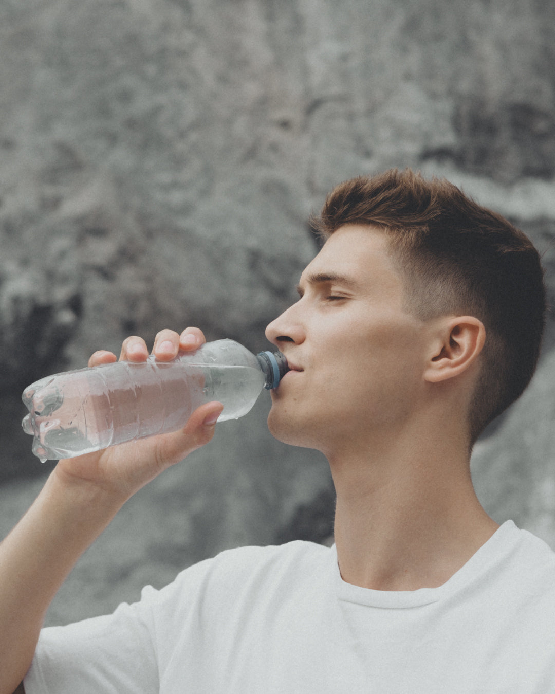 Junger Mann, der aus einer Flasche trinkt.