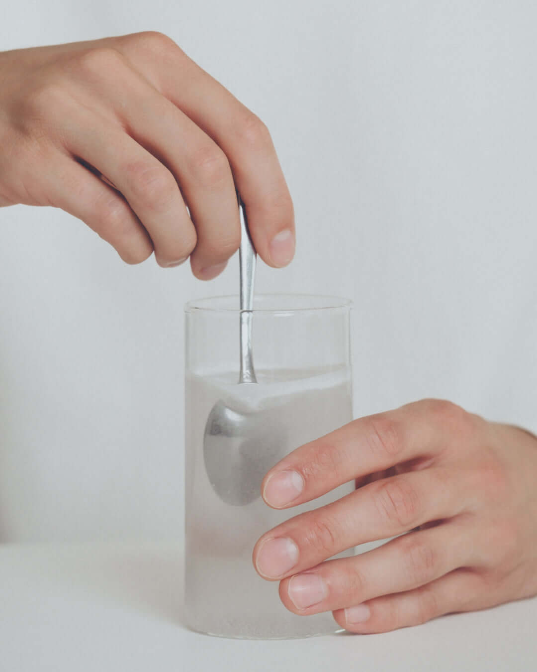 Nahaufnahme von Händen, die einen Löffel in einem Glas mit Wasser umrühren.