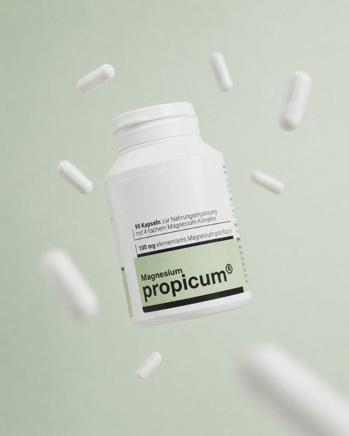 Eine grün weiße Plastikverpackung mit propicum Magnesium schwebt vor einem hellgrünen Hintergrund. Drum herum fliegen weiße Kapseln.