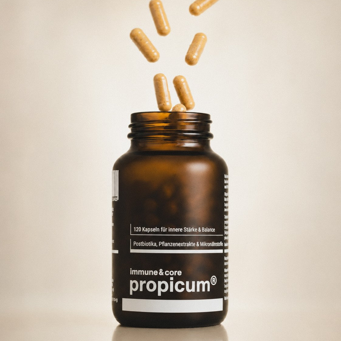 Kurkumafarbene Kapseln fallen in einen braunen Glasbehälter mit propicum immune & core