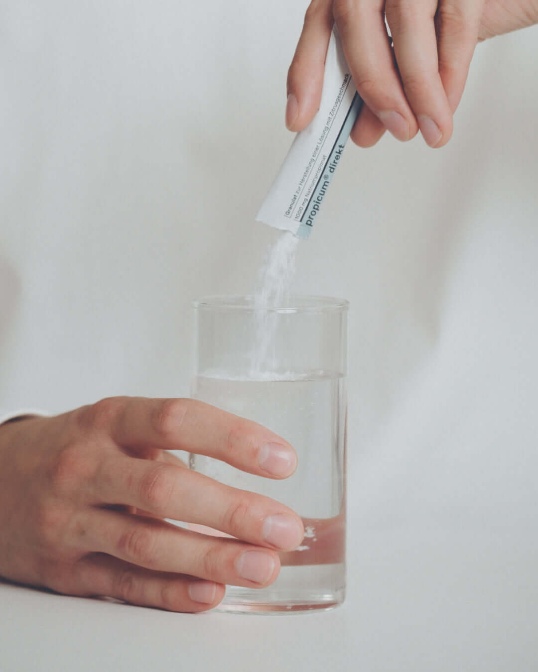 Hand gießt Pulver aus einem Sticksachet 'propicum direkt' in ein Glas Wasser – Nahrungsergänzungsmittel mit Zitrusgeschmack zur Stärkung des Immunsystems, löslich für eine einfache Einnahme.