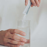 Hand gießt Pulver aus einem Sticksachet 'propicum direkt' in ein Glas Wasser – Nahrungsergänzungsmittel mit Zitrusgeschmack zur Stärkung des Immunsystems, löslich für eine einfache Einnahme.